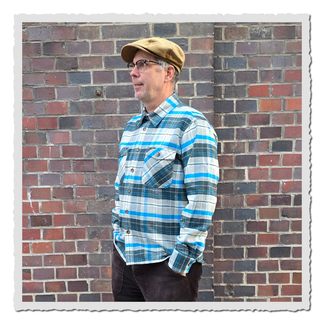 Mann vor Ziegelwand trägt Pike Brothers 1943 CPO Shirt Barrow Green – klassisches Flanellhemd